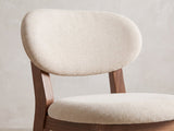 Close-up of the Caccuri 63-Inch Sintered Stone Walnut-Finish Dining Set with 4 Chairs: the oval padded back and round seat of a chair in ivory-beige chenille