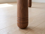 Close-up of the Caccuri 63-Inch Sintered Stone Walnut-Finish Dining Set with 4 Chairs: a cylindrical walnut-finish leg with three incised rings above its rounded foot
