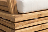 Close-up of the solid acacia on a Calamosche club chair: stacked boards with natural grain and end grain at the corner, under the ivory seat cushion