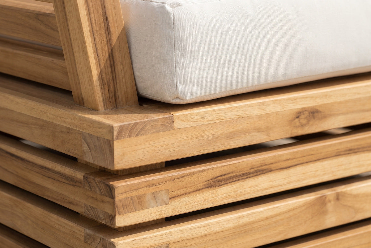 Close-up of the solid acacia on a Calamosche club chair: stacked boards with natural grain and end grain at the corner, under the ivory seat cushion