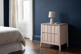 Calangianus whitewash plank two-drawer nightstand with a ceramic lamp beside a bed in a Brooklyn brownstone bedroom with a deep navy plaster wall and a herringbone parquet floor
