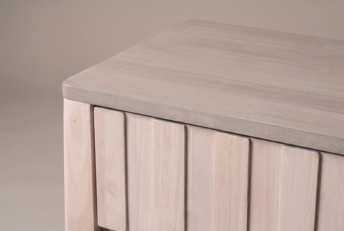 The top drawer of the Calangianus nightstand: narrow vertical planks with no handle, beside the rounded corner of the grey-washed top