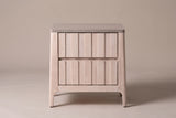 The Calangianus nightstand in pale whitewashed hardwood, front view on a warm greige studio backdrop: two nine-plank drawer fronts, a grey-washed top and four leaning legs
