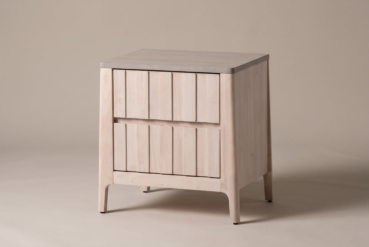 The Calangianus two-drawer nightstand in pale whitewashed hardwood with nine-plank drawer fronts and a grey-washed top, three-quarter view on a warm greige studio backdrop