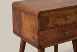 The front corner of the Calasetta nightstand: the top rolling over a rounded corner of curved mango blocks, two flush drawers with their brass knobs and the top of a tapered leg