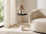 Calimera Black Mango and Marble Pedestal Side Table with a lamp and a ceramic bowl beside a cream boucle armchair in a bright plaster room