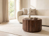 Camaiore Faceted Mango Drum Coffee Table styled with books, a vase and a stone bowl in front of a cream sofa in a bright plaster room