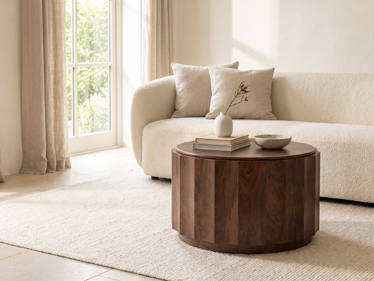 Camaiore Faceted Mango Drum Coffee Table styled with books, a vase and a stone bowl in front of a cream sofa in a bright plaster room