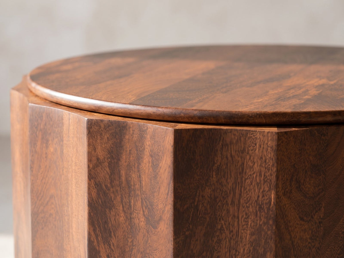 Close-up of the Camaiore Faceted Mango Drum Coffee Table: the rounded edge of the top over the faceted drum