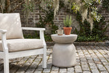 Cammarata light grey concrete dish-top bell side table with a stoneware mug and a pot of rosemary beside a white wooden armchair on granite cobbles in a Savannah, Georgia courtyard, an old grey brick wall and Spanish moss behind (chair and decor not included)