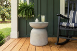 Cammarata light grey concrete dish-top bell side table with a glass of lemonade and a white bud vase beside a black rocking chair on a heart pine porch in Wilmington, North Carolina, a forest-green board-and-batten wall behind (chair and decor not included)