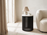 Camogli Marble and Black Metal Drum Side Table with a lamp and a ceramic bowl beside a cream boucle armchair in a bright plaster room