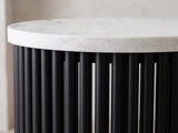 Close-up of the Camogli Marble and Black Metal Drum Side Table: the white marble top edge over the round black metal tubes