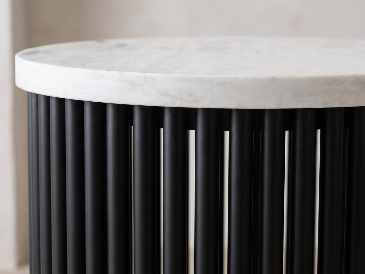 Close-up of the Camogli Marble and Black Metal Drum Side Table: the white marble top edge over the round black metal tubes