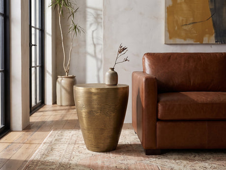 Capestrano Antique Brass Cast Aluminum Drum Side Table beside a leather sofa in an industrial loft