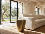 Capestrano Antique Brass Cast Aluminum Drum Side Table beside a linen sofa in a poolside villa