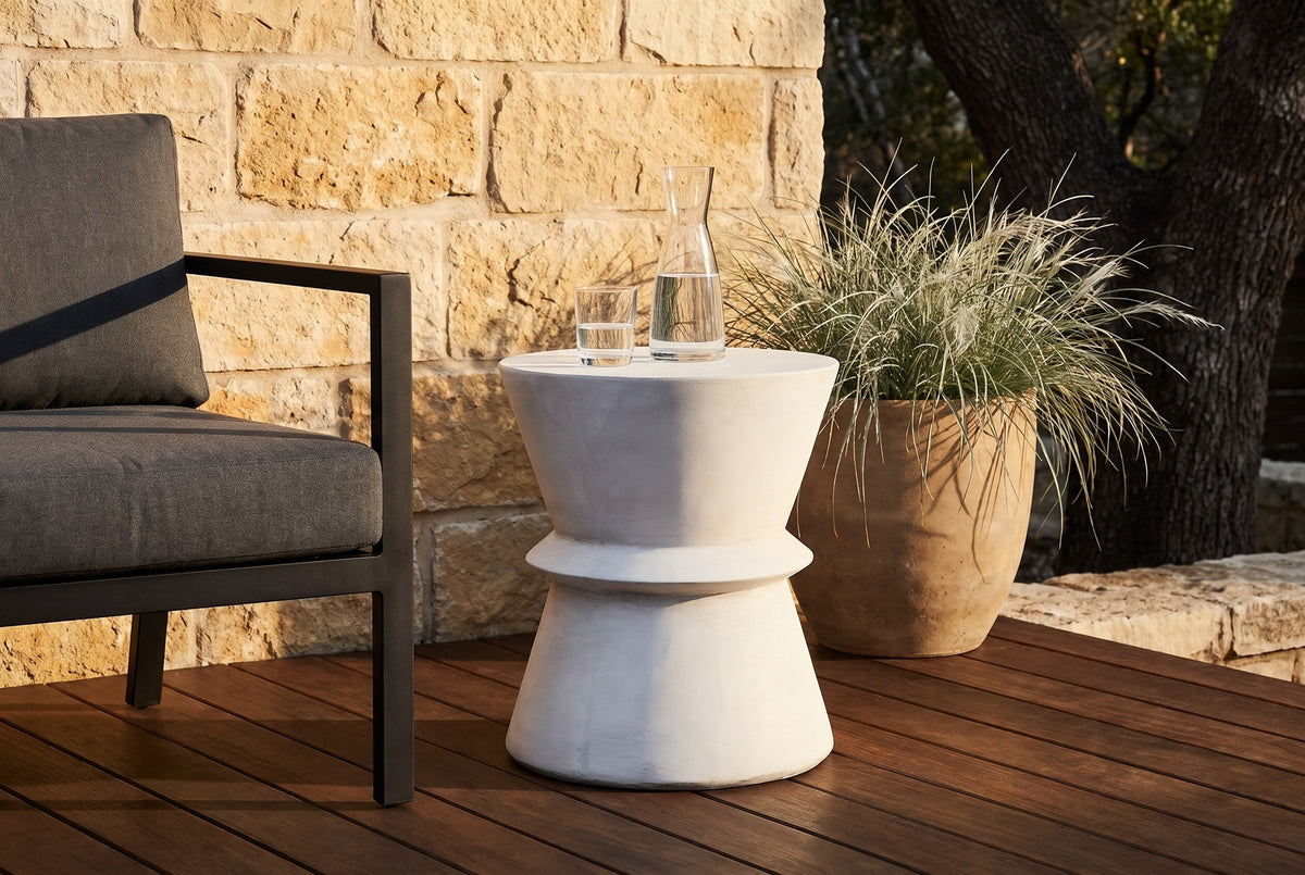 Capizzi antique white concrete side table on a dark ipe deck in front of a honey limestone wall near Austin, beside a black steel club chair (chair and carafe not included)