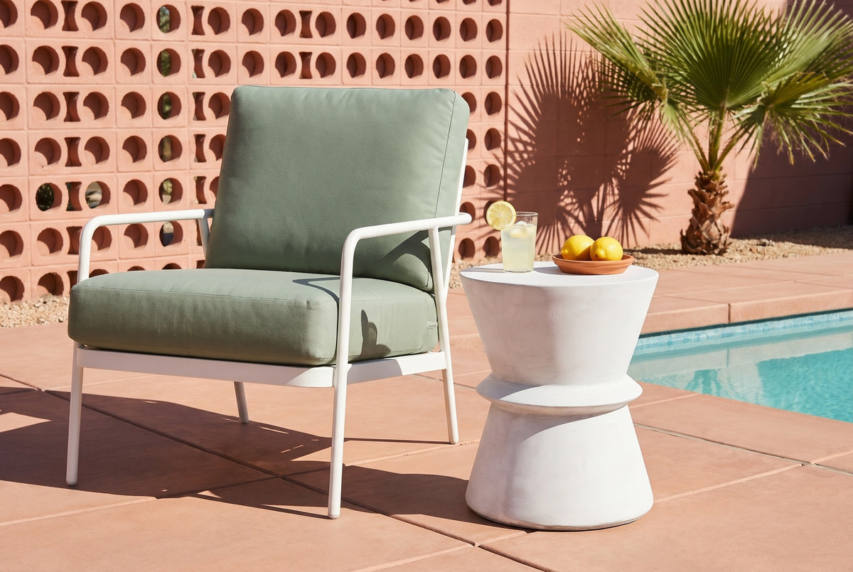 Capizzi concrete side table on terracotta tiles by a pool in Palm Springs, a pink breeze-block wall and a fan palm behind, beside a white lounge chair with a sage cushion (chair and decor not included)