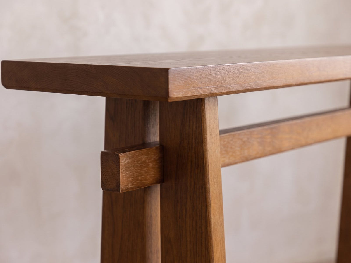 Close-up of the Capurso Wood Veneer Trestle Console Table: the beam passing through a slab leg under the thick top