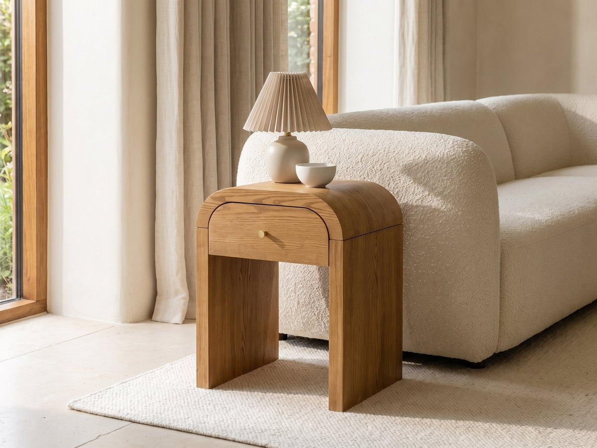 Cariati Ash Veneer Curved-Top Side Table with a lamp and a ceramic bowl beside a cream boucle sofa in a bright plaster room
