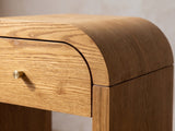 Close-up of the Cariati Ash Veneer Curved-Top Side Table: the rounded shoulder of the top over the drawer and gold-tone knob