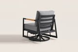 The Carini chair from behind: the black aluminum back frame with three wide slats, the gray back cushion, one teak arm and the swivel glider base