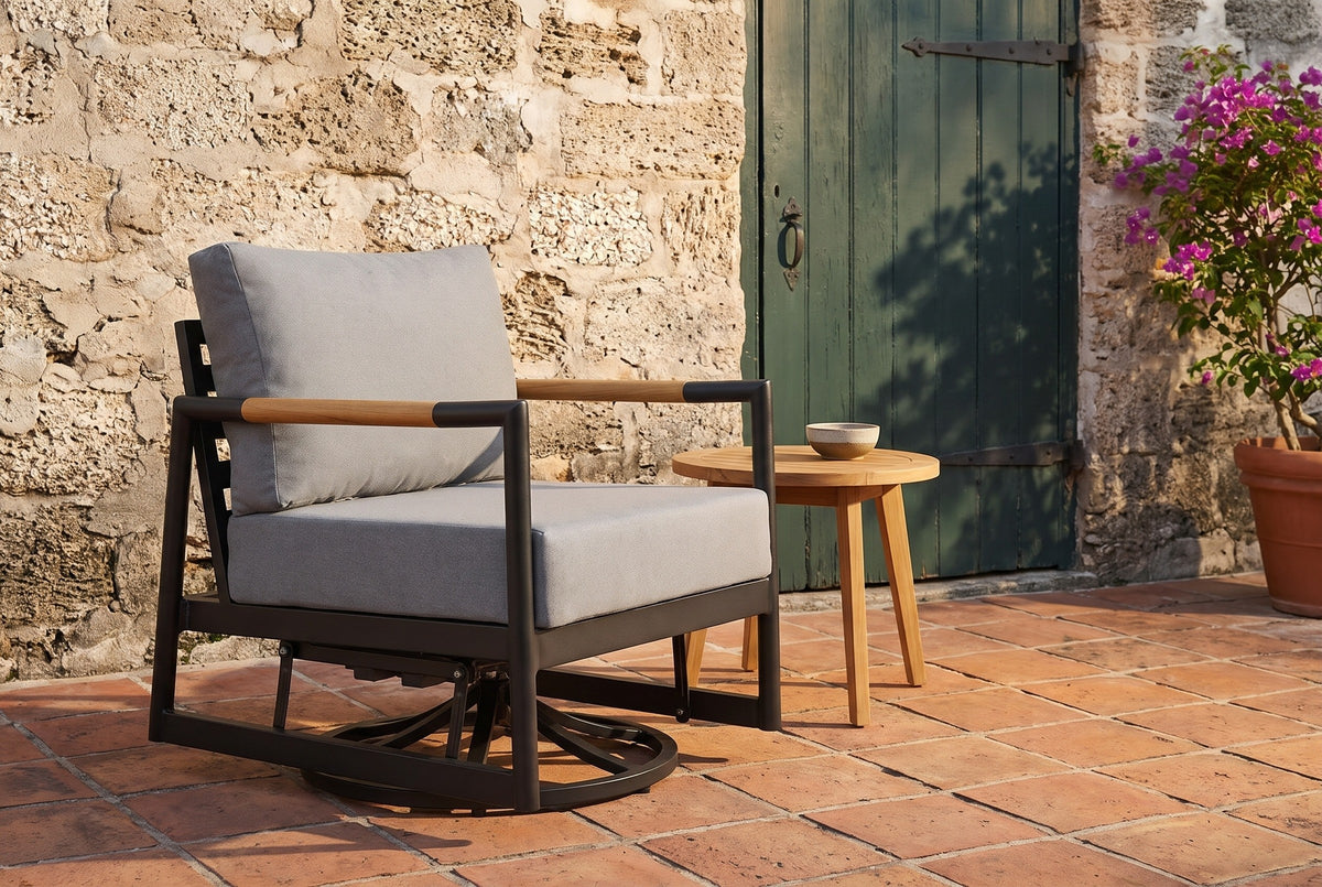 The Carini swivel glider lounge chair on an old terracotta tile terrace in St. Augustine, a coquina shell-stone wall and a green wooden door behind (side table and bowl not included)