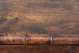 Close-up of the roasted almond mango wood on the Carloforte nightstand: dark brown grain with a golden patch above a turned bamboo rail with raised rings