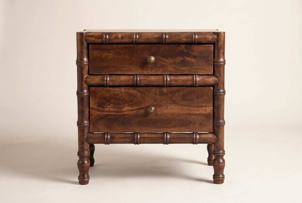 The Carloforte nightstand in roasted almond mango, front view on a light studio backdrop: three bamboo rails, two drawers with brass knobs and four turned legs