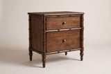 The Carloforte nightstand in roasted almond mango with a faux-bamboo frame, two drawers with brass knobs and four turned legs, three-quarter view on a light studio backdrop