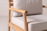 Close-up of the solid acacia on the Caronia chair: the round arm rail meeting the round front leg, with the beige cushions beside it