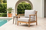 Caronia acacia club chair on a travertine pool deck in front of a white stucco wall with an arched opening and a clipped hedge (side table not included)