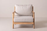 The Caronia club chair seen from the front: round arm rails, round legs, the flat seat frame and beige cushions