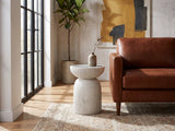 Casarano Fiber Concrete Hourglass Side Table beside the arm of a cognac leather seat in an industrial loft