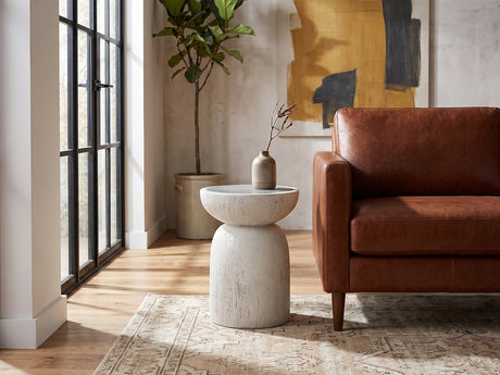 Casarano Fiber Concrete Hourglass Side Table beside the arm of a cognac leather seat in an industrial loft