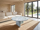 Cascia Compact Blue-Grey Marble Coffee Table seen from the side, on a jute rug in front of a linen sofa in a poolside villa
