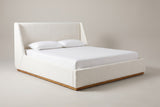 The Casoli bed in white boucle on a natural wood plinth with a white mattress and pillows (not included), three-quarter view on a light studio backdrop