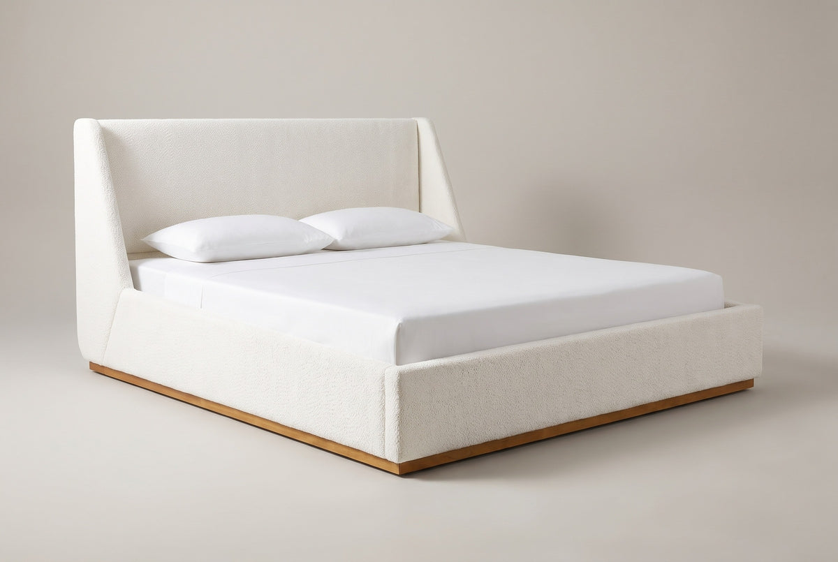 The Casoli bed in white boucle on a natural wood plinth with a white mattress and pillows (not included), three-quarter view on a light studio backdrop
