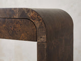 Close-up of the Castellana Burl Veneer Waterfall Console Table: the rounded bend where the burl top curves down to meet a leg, beside the curved corner of a drawer