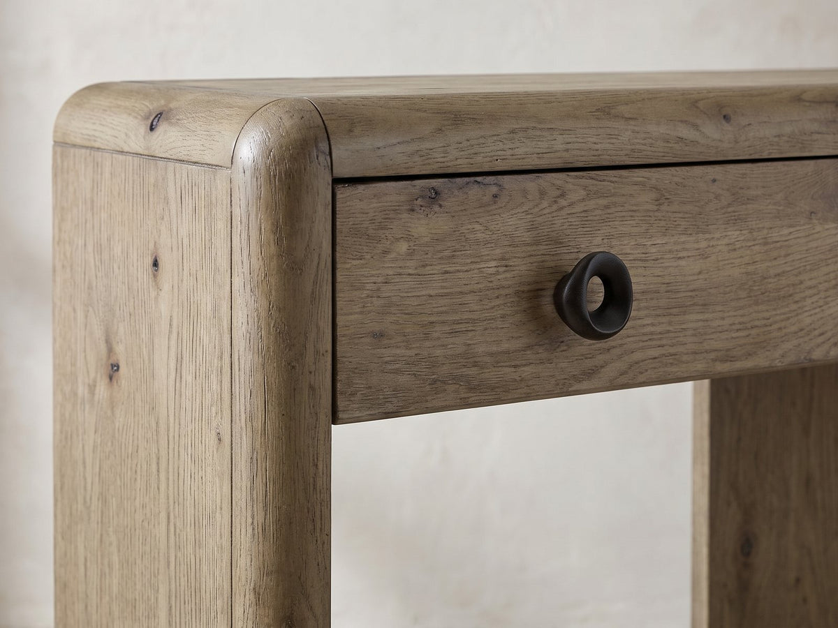 Close-up of the Castellaneta Knotty Oak Veneer Console Table: the rounded top corner of an end panel beside a drawer with its dark ring pull