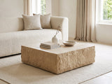 Castellina Faux Travertine Fiberglass Block Coffee Table styled with books, a vase and a stone bowl in front of a cream sofa in a bright plaster room