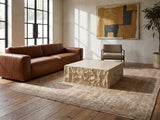 Castellina Faux Travertine Fiberglass Block Coffee Table seen from the side, on a vintage rug in front of a leather sofa in an industrial loft