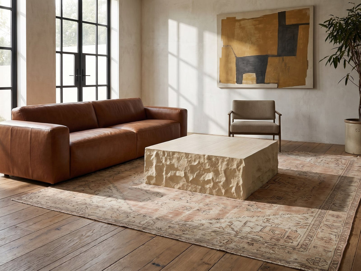 Castellina Faux Travertine Fiberglass Block Coffee Table seen from the side, on a vintage rug in front of a leather sofa in an industrial loft