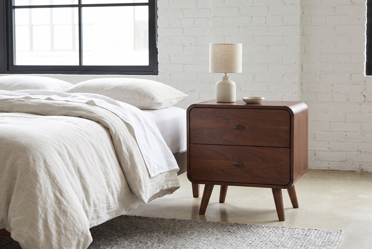Castelsardo dark walnut nightstand with a ceramic lamp against a white-painted brick wall in a Chicago loft bedroom with a polished concrete floor and a black steel window