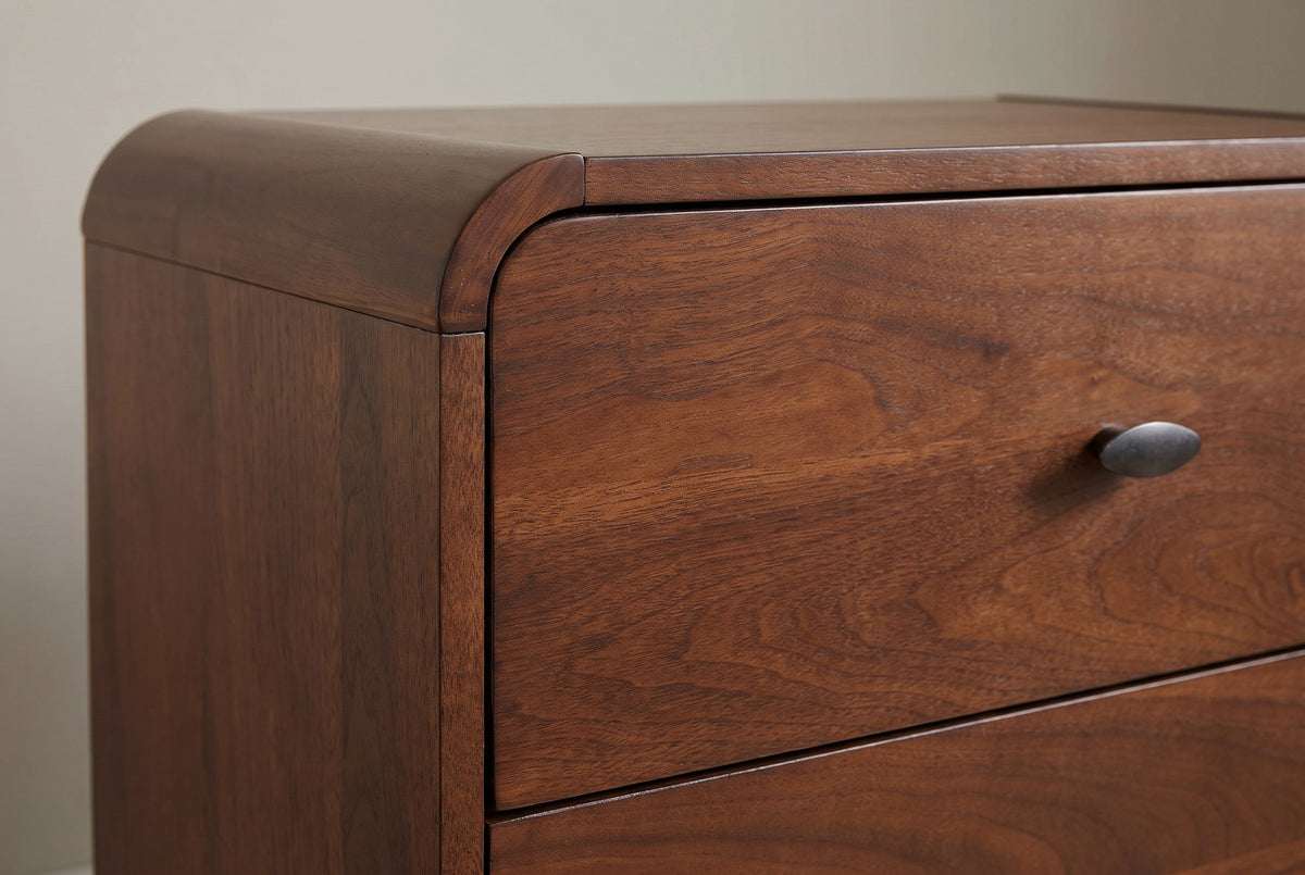 The top drawer of the Castelsardo nightstand with its oval gunmetal pull, beside the thick rounded rail at the corner of the top