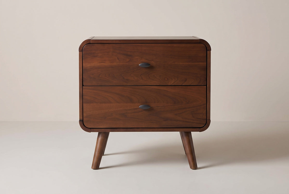 The Castelsardo nightstand in dark walnut veneer, front view on a light greige studio backdrop: two drawers with oval pulls, rounded corners and four splayed legs