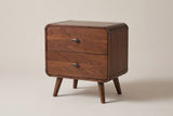 The Castelsardo two-drawer nightstand in dark walnut veneer with rounded rails, oval gunmetal pulls and splayed round legs, three-quarter view on a light greige studio backdrop