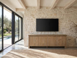 Cefalu Fluted Oak Media Console under a wall-mounted screen on a pale stone wall in a poolside villa