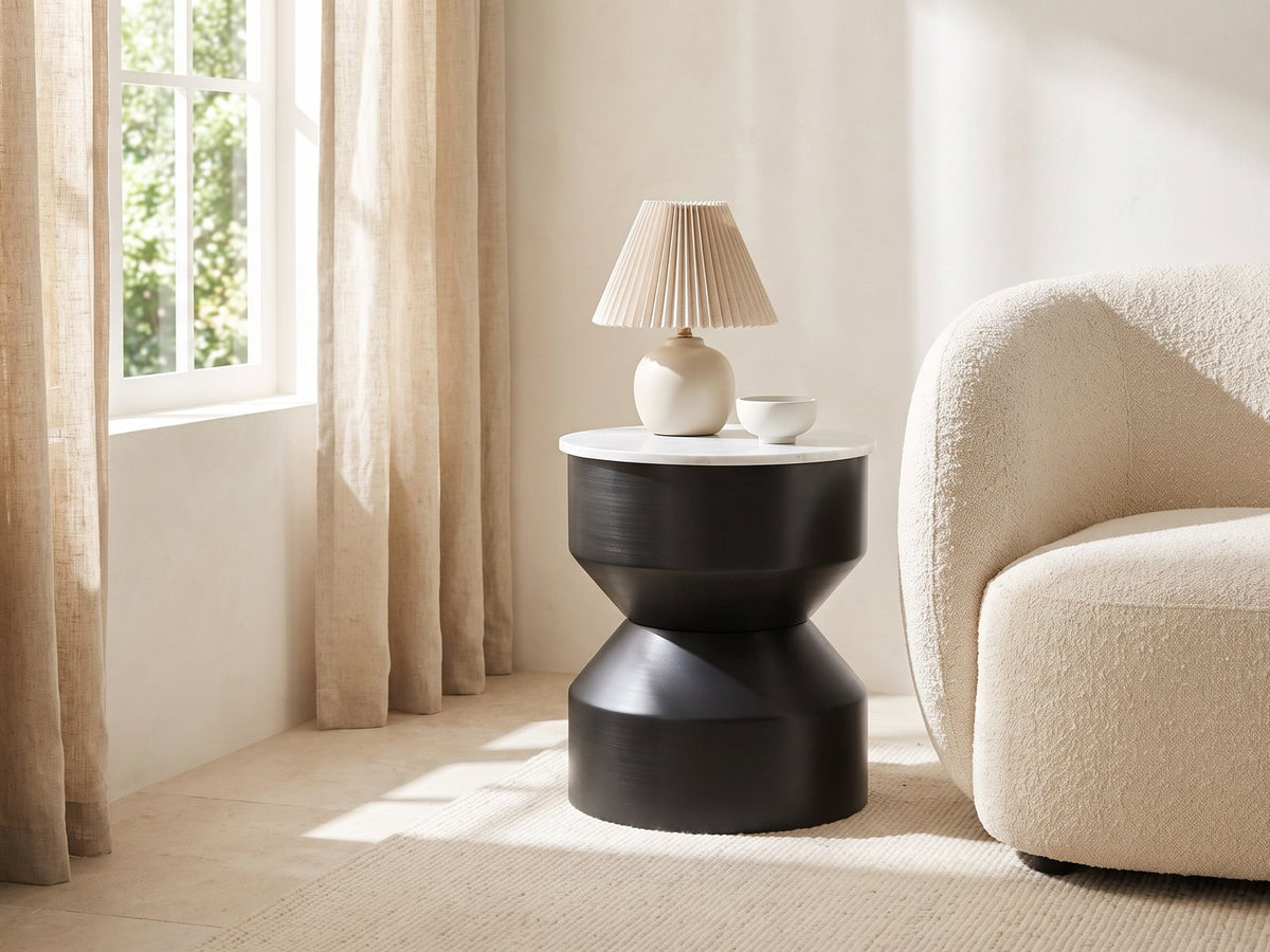 Ceglie White Marble Hourglass Side Table with a lamp and a ceramic bowl beside a cream boucle armchair in a bright plaster room