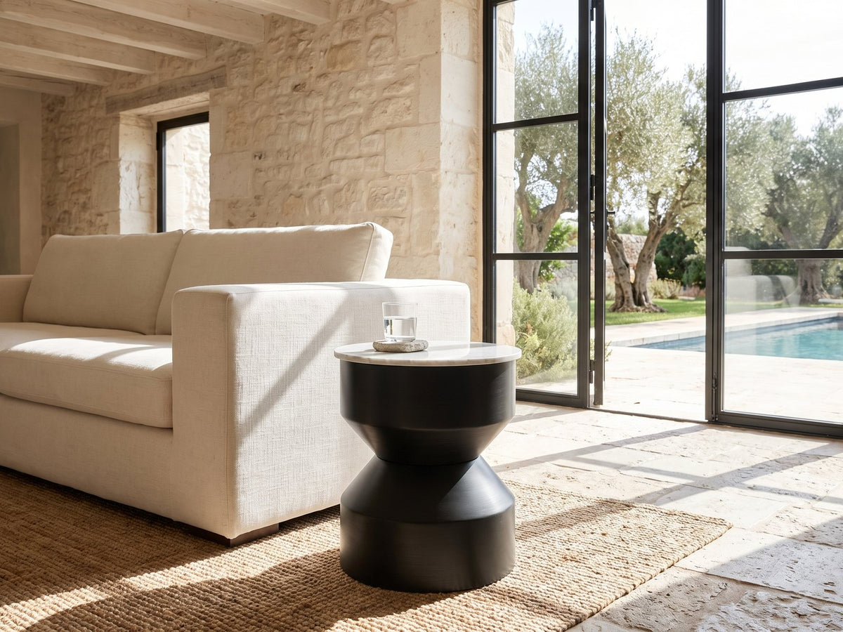 Ceglie White Marble Hourglass Side Table beside a linen sofa in a poolside villa